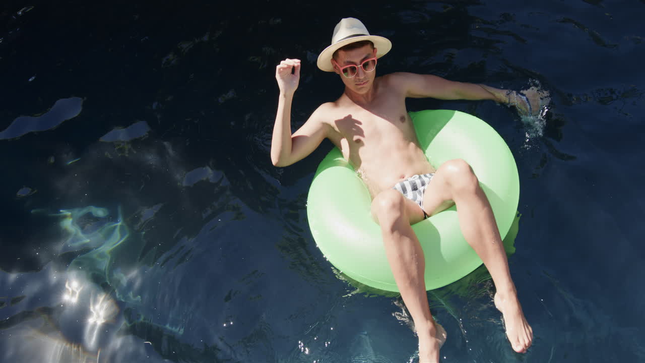 Young man enjoys a relaxing day floating in a pool, with copy space