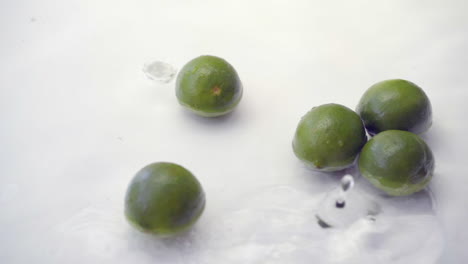 slomo of limes falling into water on white backdrop