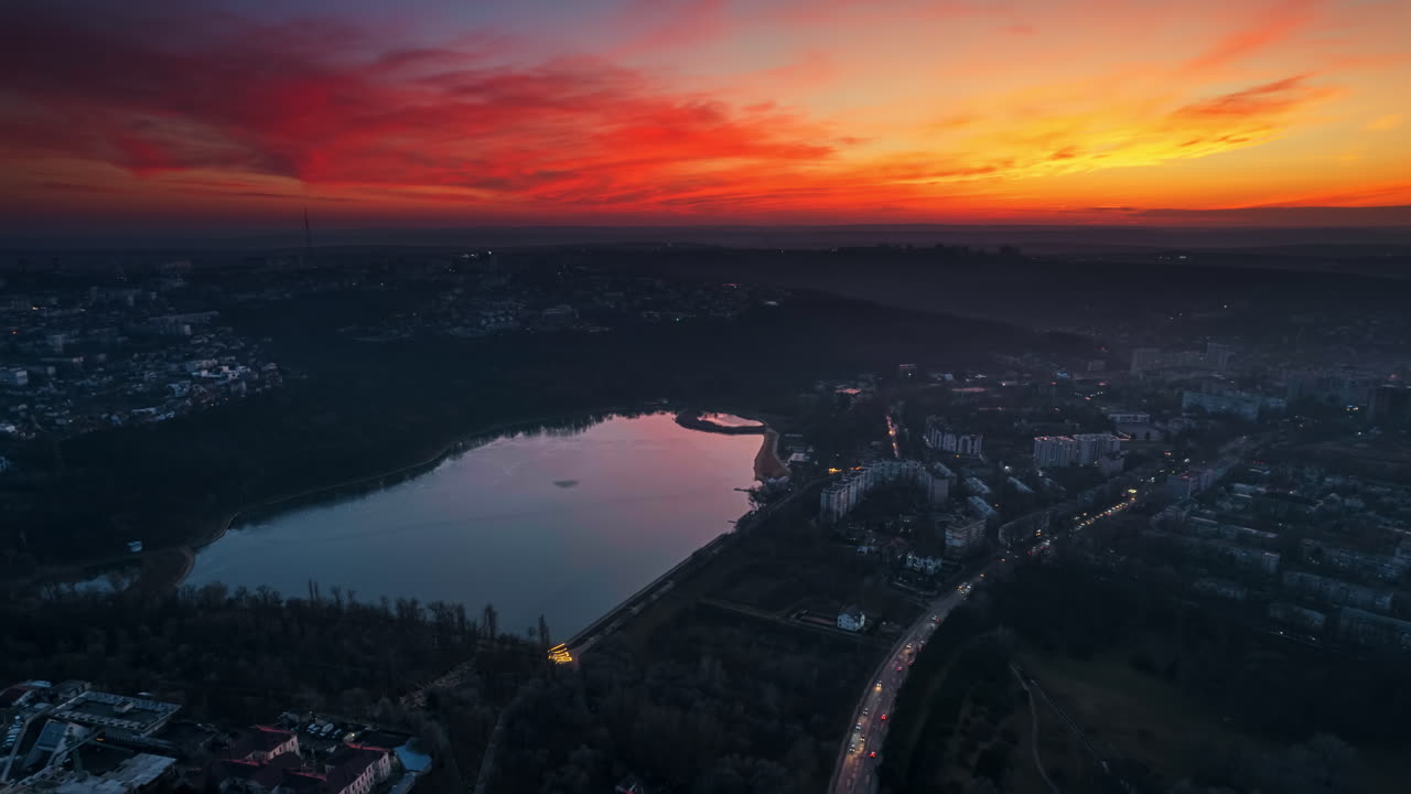 Aerial drone timelapse view of Chisinau at sunset, Moldova. View of city centre with lake, buildings, roads, illumination