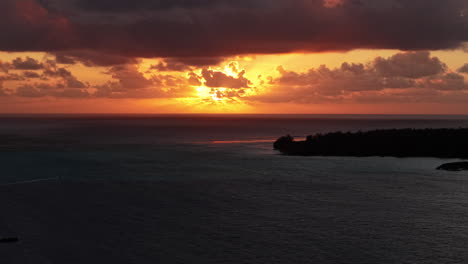 aerial view of sunset above bora bora island lagoon and clouds on south pacific ocean horizon, french polynesia