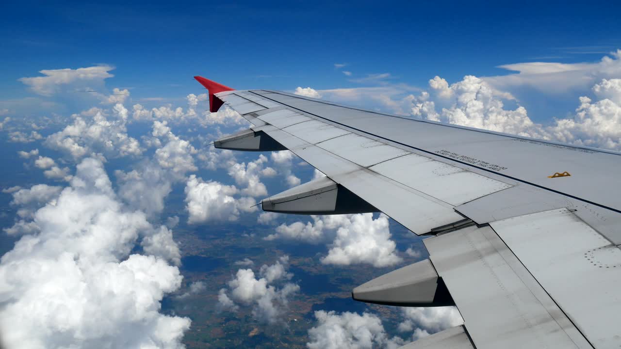 Filmagem 4K. Viajando de avião. Vista aérea através da janela de um avião. Asa de avião e belas nuvens brancas no céu azul para fundo de viagem.