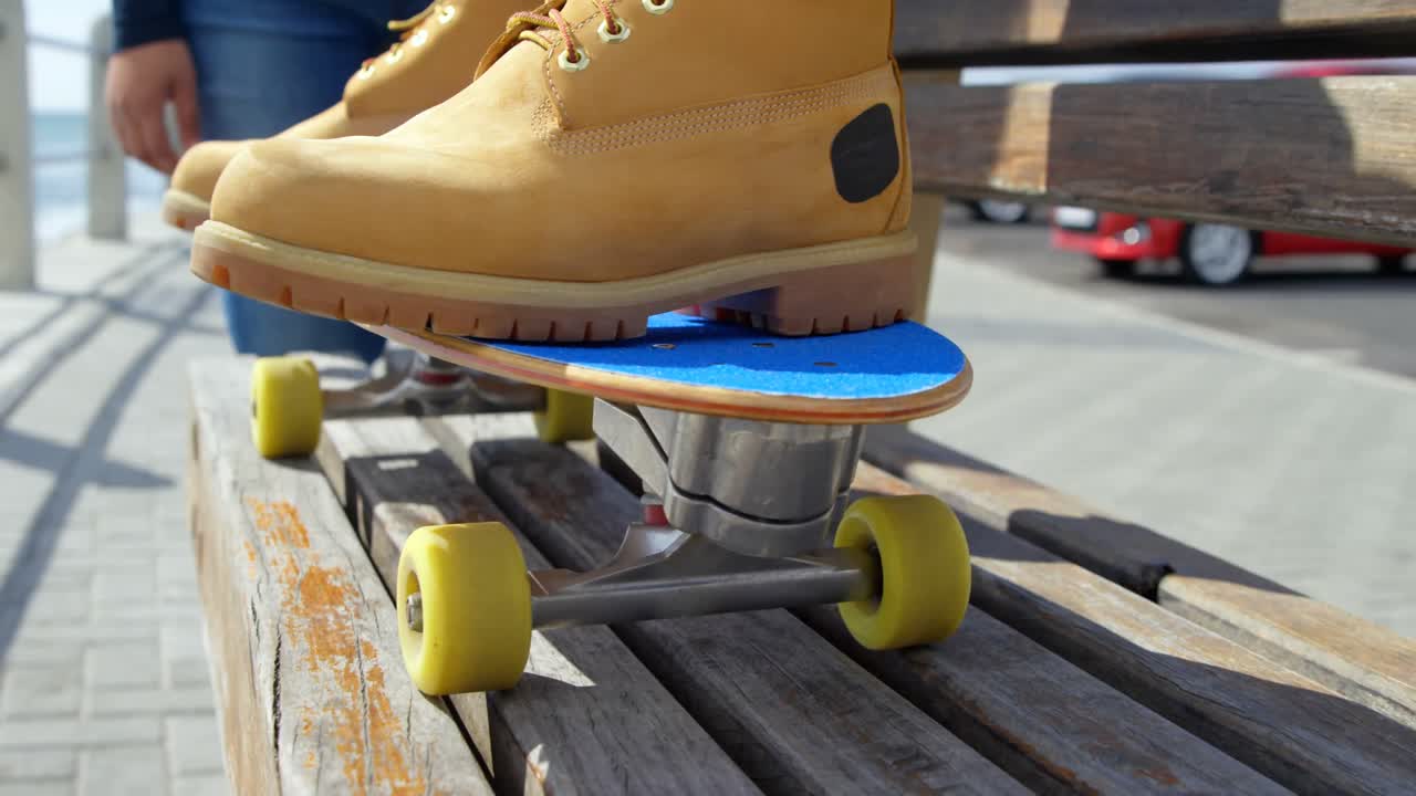 Close-up of man sitting on skateboard near beach 4k