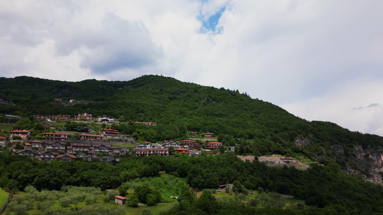 Hillside neighborhood with dense tree cover and scattered houses under a dramatic cloudy sky in Riva di Solto, Bergamo, Italy Italia