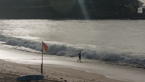 Pequeñas-Olas-Ruedan-Hacia-La-Orilla-Mientras-Un-Hombre-Corre-Hacia-Las-Olas-A-Lo-Largo-De-La-Costa-Oeste-De-Los-EE.UU.