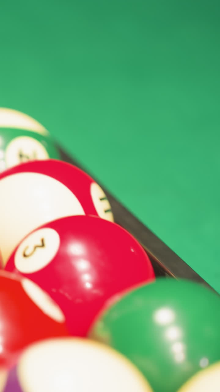 Une personne portant une chemise blanche et un pantalon gris récupère une boule verte dans un trou d’une table de billard verte. Un gros plan capture le mouvement de la main, la texture de la table de billard et l’interaction du jeu dans une faible lumière.
