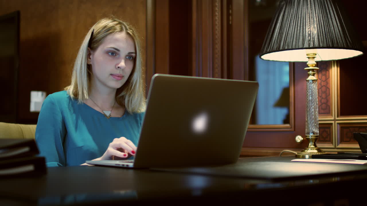 Business woman opening notebook computer for working on desk with table lamp