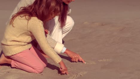 mother and daughter writing on sand