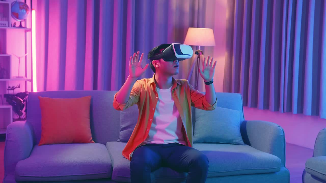 Giovane uomo asiatico che esplora la realtà virtuale in salotto, con colori ciano e magenta