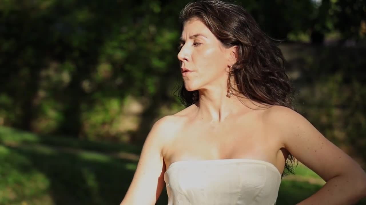Woman in white strapless dress practicing flamenco choreography in park at sunset