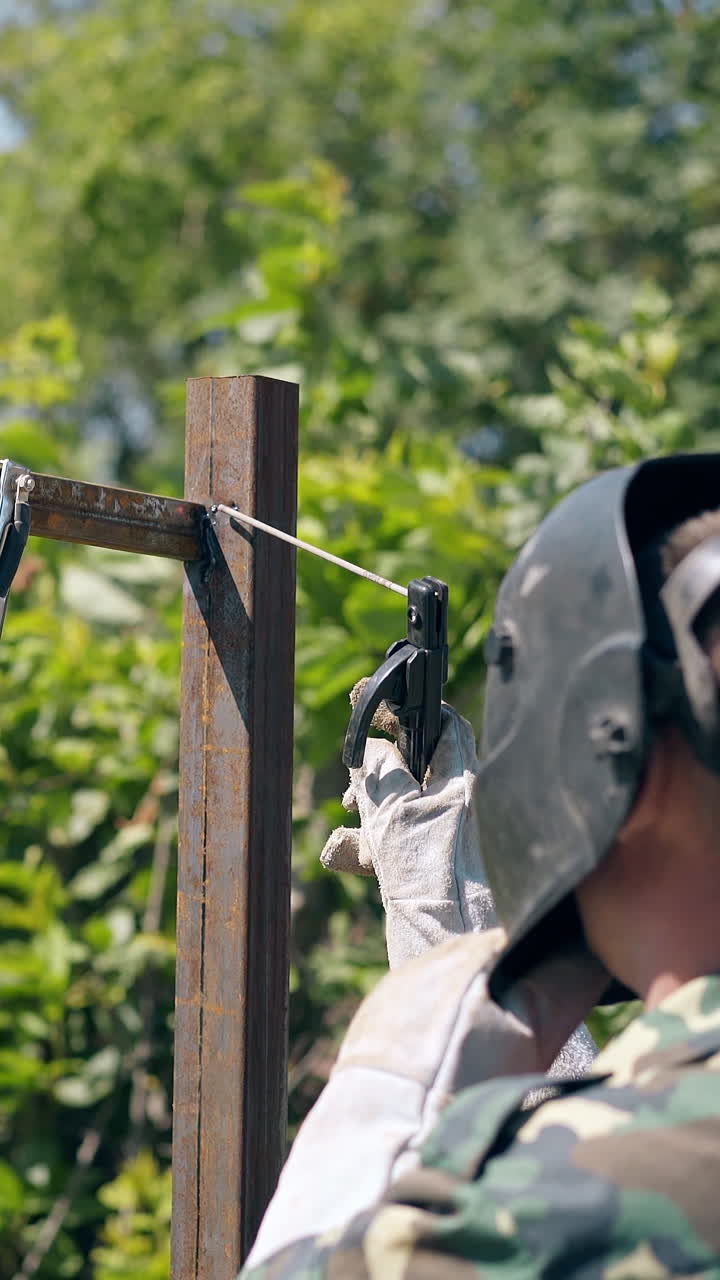 skilled craftsman in protective mask welds upper detail to fence pole with compact instrument in garden