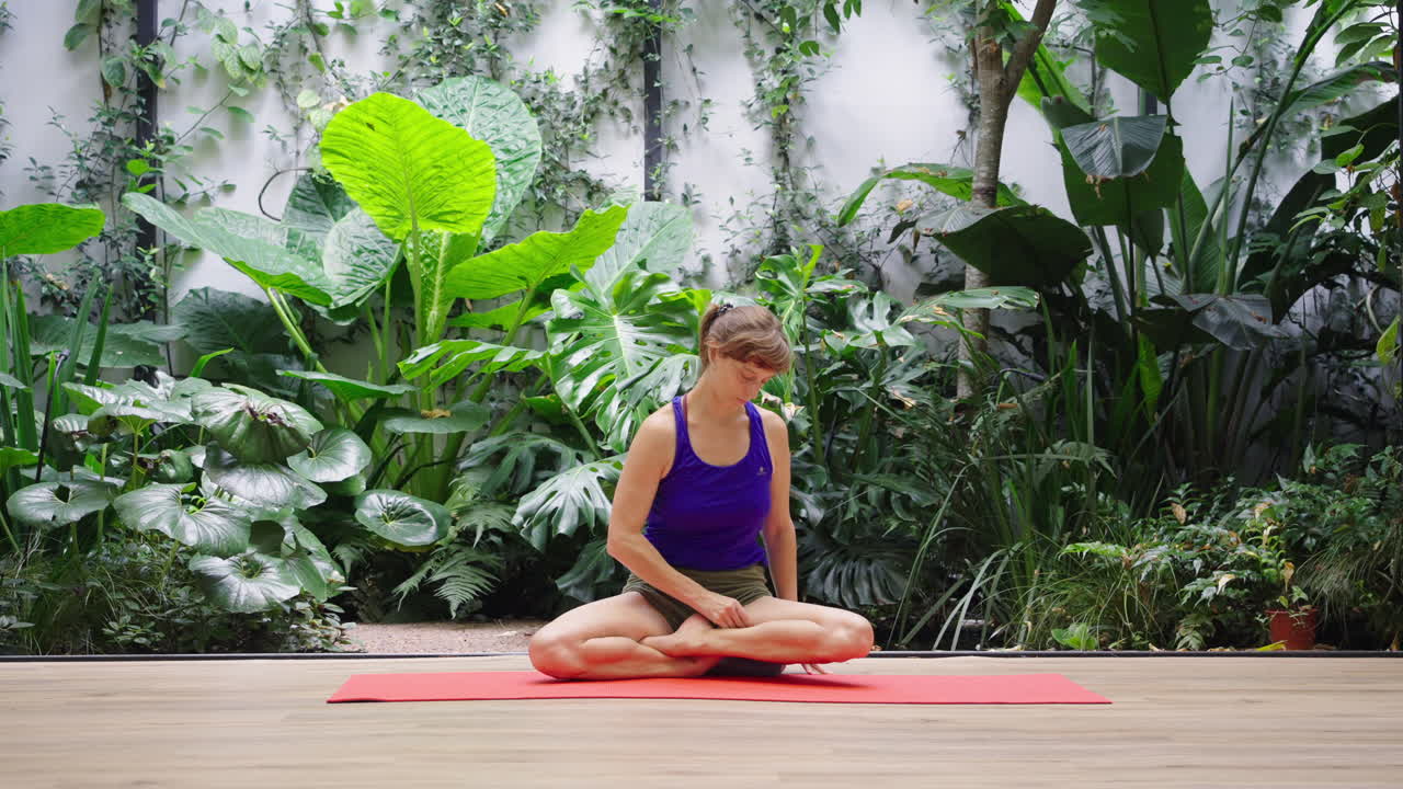 Woman Sits in Lotus Position on Yoga Mat in Indoor Garden