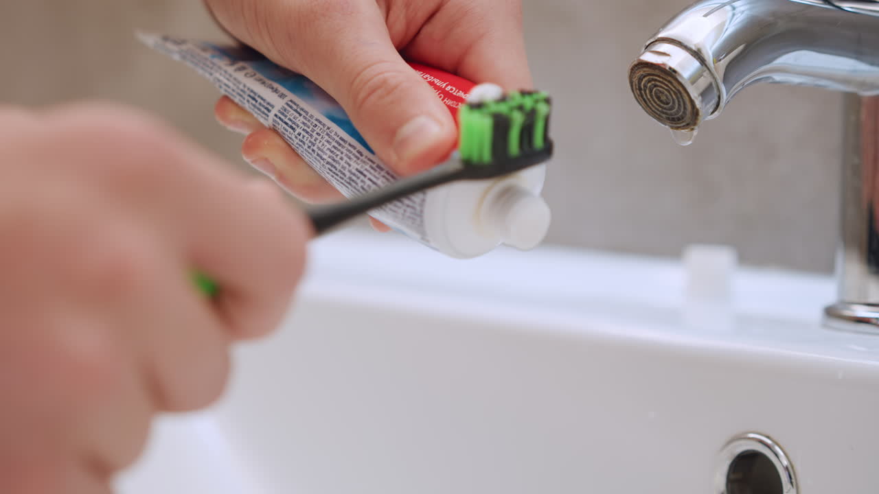 Closeup hands holding brush under faucet independent practice vibe precise paste application steady grip on green bristles domestic bathroom morning light focus on motion and skill