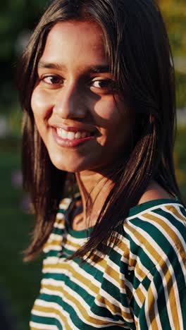 golden hour sunlight illuminates a young woman with long dark hair, wearing a striped shirt, as she poses with various facial expressions in a garden setting