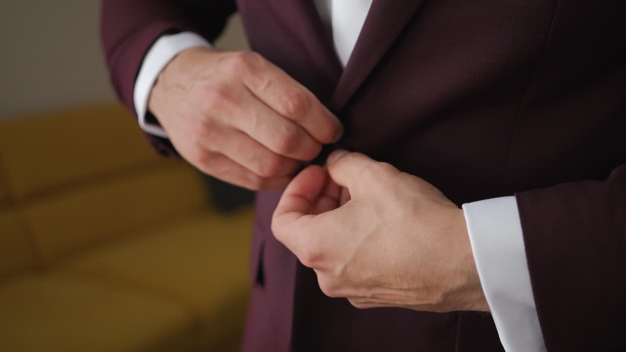 Close-up shot of the groom's hand fastening a button on a velvet jacket