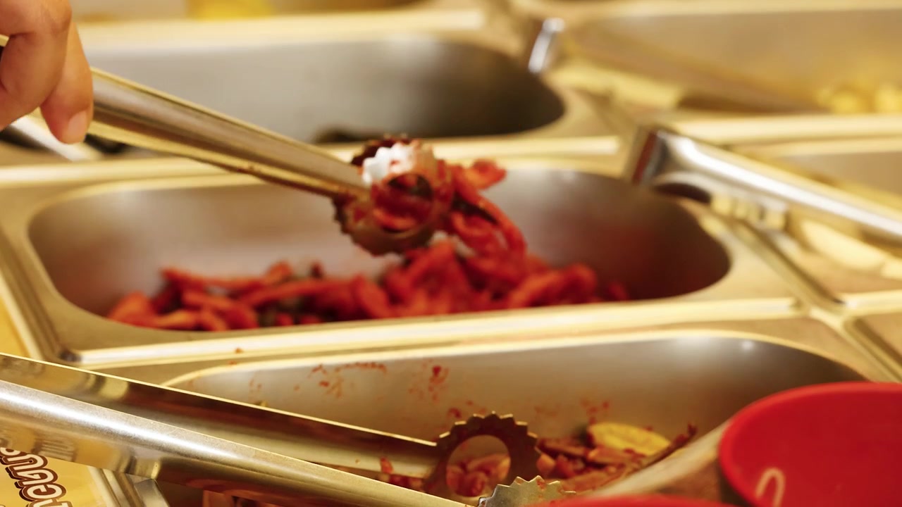 Primo piano di una mano che usa pinze di metallo per servire kimchi coreano da un vassoio da ristorante