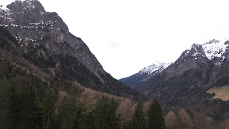 drone rise up to summit cross towards snow covered mountains surrounded with pine forest in austria