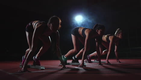 female runners at athletics track crouching at the starting blocks before a race. in slow motion.