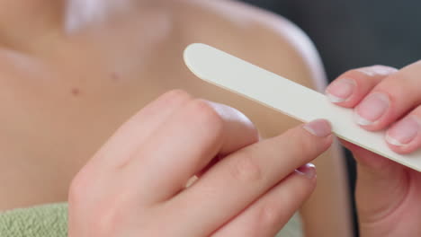 close up hand view of woman gently filing fingernails with white nail filer while wearing green towel indoors, highlighting clean nail care, feminine grooming routine, and personal hygiene focus