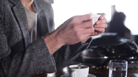 close up at the hands of a man sitting in a cafe while reading a small paper and then putting it inside a pocket in his jacket
