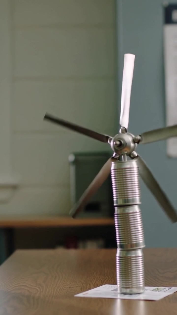 Vertical video: Placing child in navy top holding tin cans on school desk, flicking rotor for class