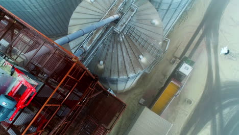 high huge containers at the modern elevator plant. drone footage over the tops of tanks and metal tower with equipment. top view of a lorry unloading grain into storage.