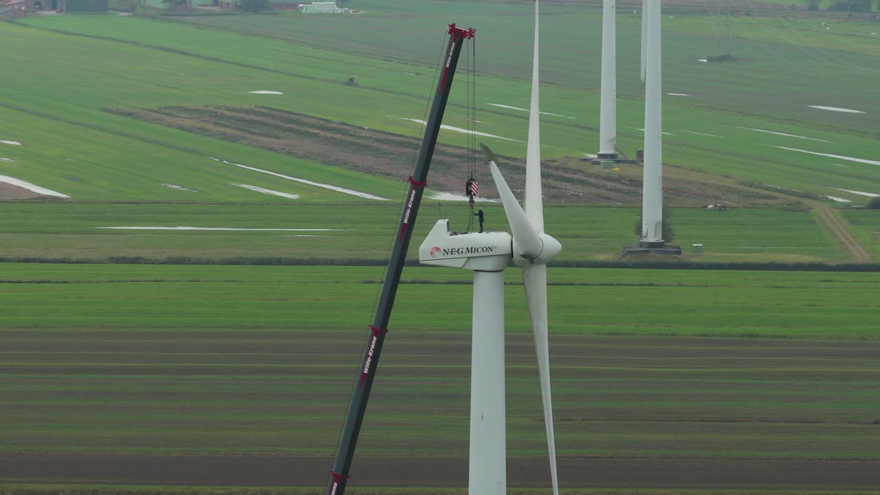 Veduta aerea di un servizio di manutenzione di turbina eolica con un membro dell'equipaggio e una gru alta.