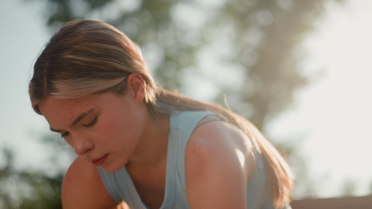 약간 구부러진 젊은 여성, 아래의 무언가에 초점을 맞추고, 빛이 그녀의 얼굴에 반사되고 머리카락이 뒤로 여, 배경에 흐릿한 초록색으로 밝은 파란색 을 입고
