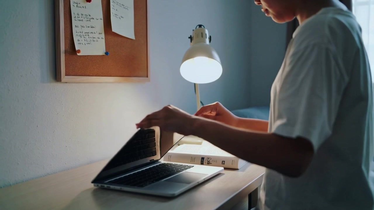 Finishing study student in tee with headset closing laptop at home desk, placing book, copy space