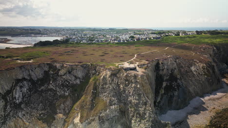 backward arc aerial reveals abandoned bunker on cliff with ocean and town in background