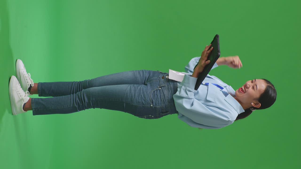 스튜디오에서 녹색 화면에서 태블릿을 사용하여 축하하는 행복한 아시아 사업가 여성의 전체 몸의 측면 시각