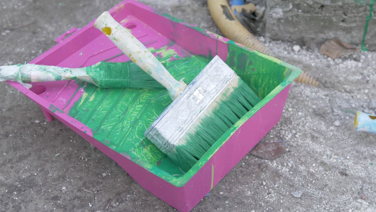 Used painters tray with brushes covered in green paint
