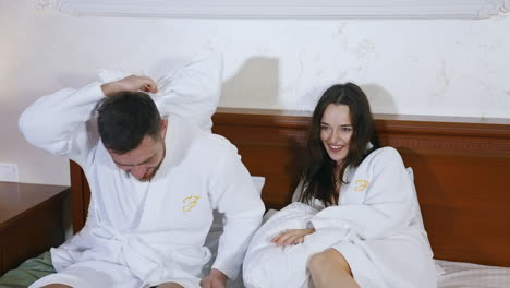 happy couple rest in hotel. woman and man in dressing gowns on bed. married couple in white coats sit comfortably on bed to watch video on a laptop.