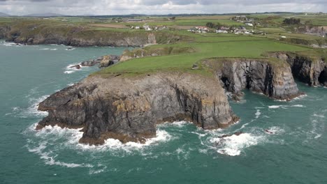 Drone-shot-of-a-small-headland-in-Ireland-with-waves-crashing-into-rocks