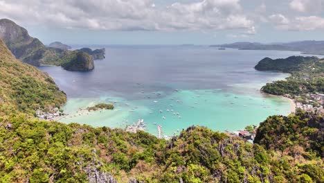 A panoramic view of El Nido, Palawan, Philippines featuring turquoise waters, limestone cliffs, boats, lush hills, and the bustling coastal town nestled between scenic landscapes and calm sea