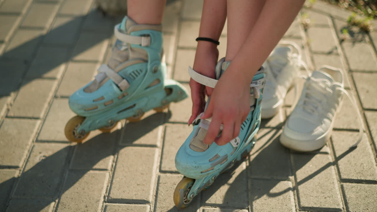 Partial view of individual adjusting roller skate strap on left leg while wearing black wrist band, white sneakers lying in background, with greenery in the background