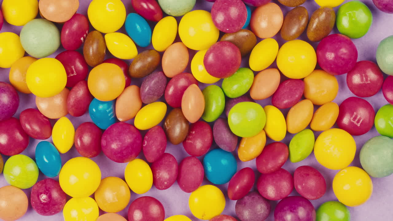 Colorful dragee candies on purple background. Summer bright texture studio shot for store, supermarket, close up top view. Children sweets made of sugar, mix of lollipops. beautiful bonbons.