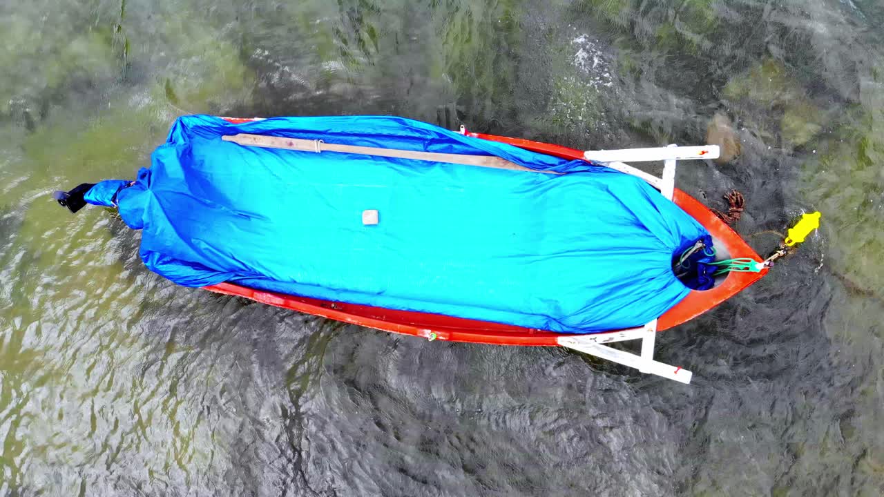 Aerial drone view of a moored boat with blue fabric on it in transparent water of the Aegean sea. Greece