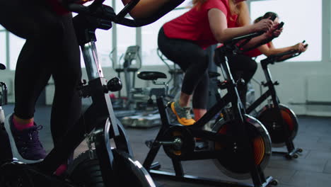 group athletic girls performing aerobic riding training exercises on cycling stationary bike in gym