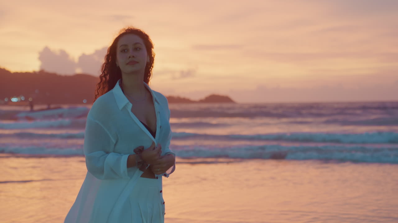 Signora in spiaggia esegue una danza elegante. Una performer si muove con ritmo delicato lungo la costa. Una donna elegante con abiti svolazzanti intrattiene con una danza vivace accanto a un tranquillo litorale al crepuscolo.
