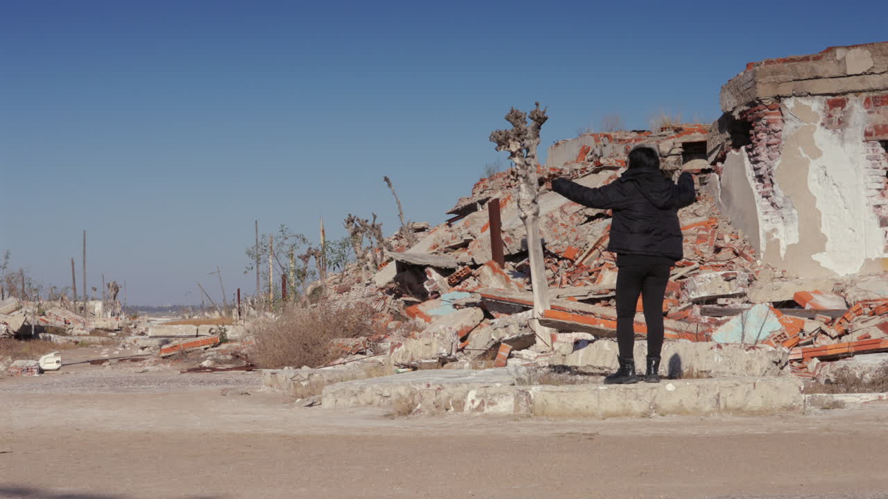 Woman raises her arms among ruined buildings, transforming a devastated space into a moment of emotional expression and inner strength, reclaiming in the aftermath of loss and personal trauma