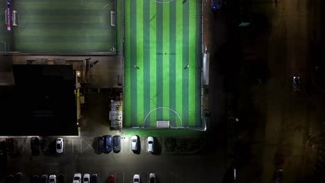 football sports facility under floodlights at night, urban area, aerial view