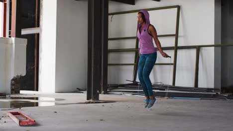 mujer afroamericana con capucha saltando con una cuerda en un edificio urbano vacío