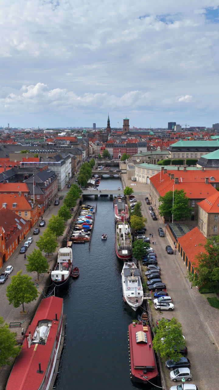 Vista aerea da drone sopra lo storico canale di Christianshavn, costeggiato da case colorate e barche ormeggiate a Copenaghen, in Danimarca. Verticale