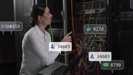 Animation-Von-Social-Media-Symbolen-über-Einer-Kaukasischen-IT-Ingenieurin-Mit-Laptop-Am-Computerserver