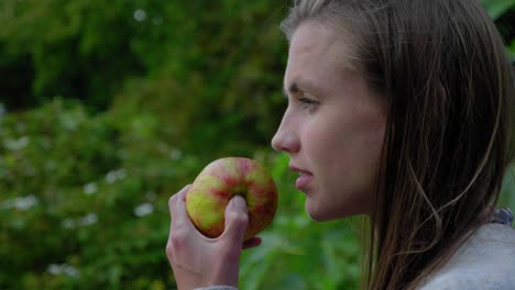 young womans bites apple and stares thoughtfully in garden, profile