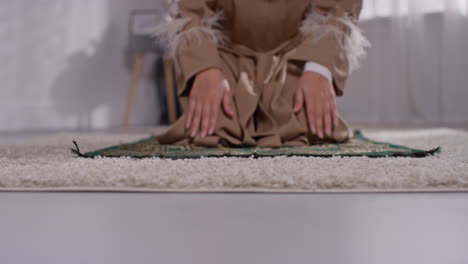 close up of muslim woman wearing hijab at home praying kneeling on prayer mat 2