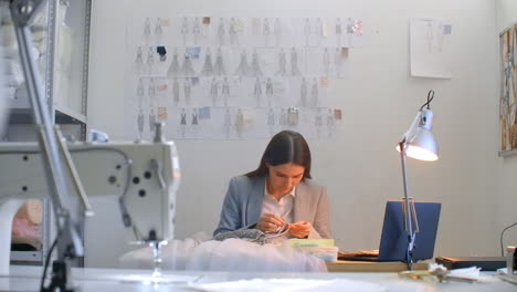 sewing workshop girl sitting at the table in hand sew beads and jewelry. sew dresses and decorate evening dresses with crystals.