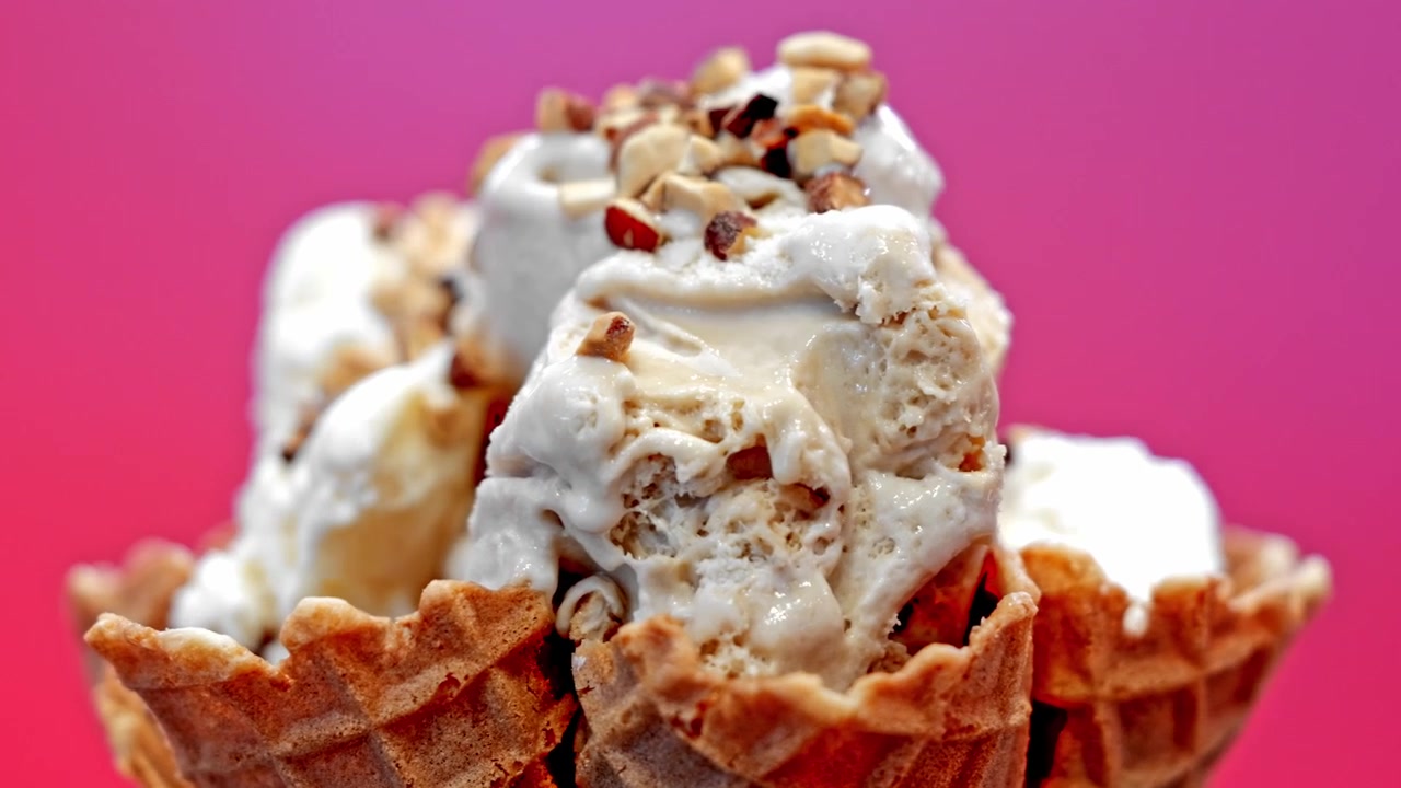 Primo piano di una grande pallina di gelato cremoso servita in un croccante cono waffle dorato, che mostra una consistenza liscia e una presentazione invitante del dessert
