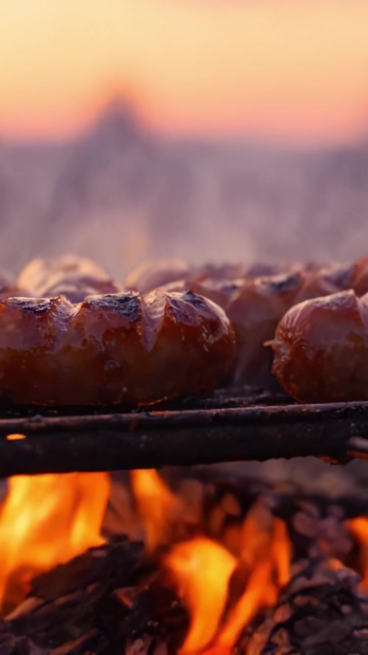 Scena di grigliata accattivante: salsicce succulente che sfrigolano su un falò ardente al crepuscolo, mostrando un ricco mix di fumo e fiamme in un sereno ambiente esterno.