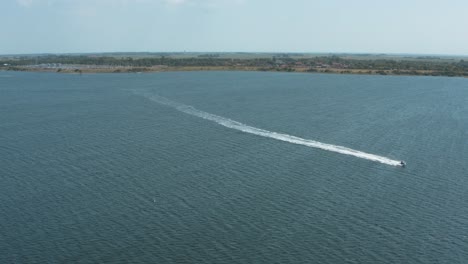 drone - aerial shot of a jetski on a blue, wavy and windy sea on a sunny day with white clouds on a island, 30p